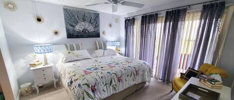 A bedroom with a bed, bedside tables, a desk, a ceiling fan, and curtains.