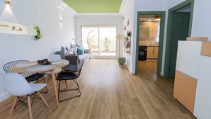 Une cuisine moderne avec un plancher en bois, un coin repas avec une table et des chaises, et une vue sur un salon équipé d’un canapé et d’un fauteuil suspendu.
