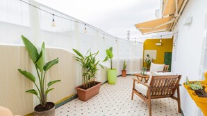 Un balcon agrémenté de plantes en pot, une chaise en bois, une petite table et un pot suspendu jaune.