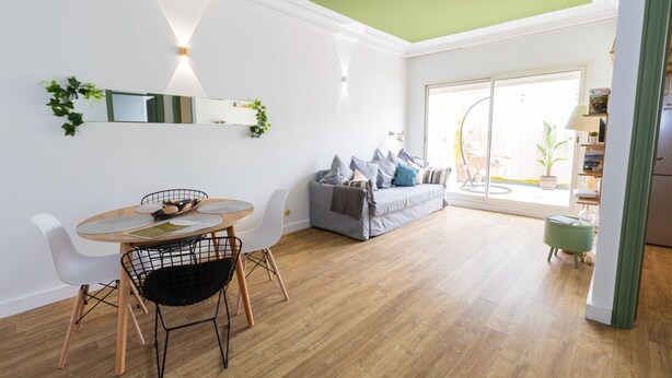 Un salon lumineux avec un coin repas, un canapé gris et un plafond vert.