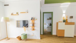 Un salon moderne avec un téléviseur, des étagères, une lampe et une petite table d’appoint verte.