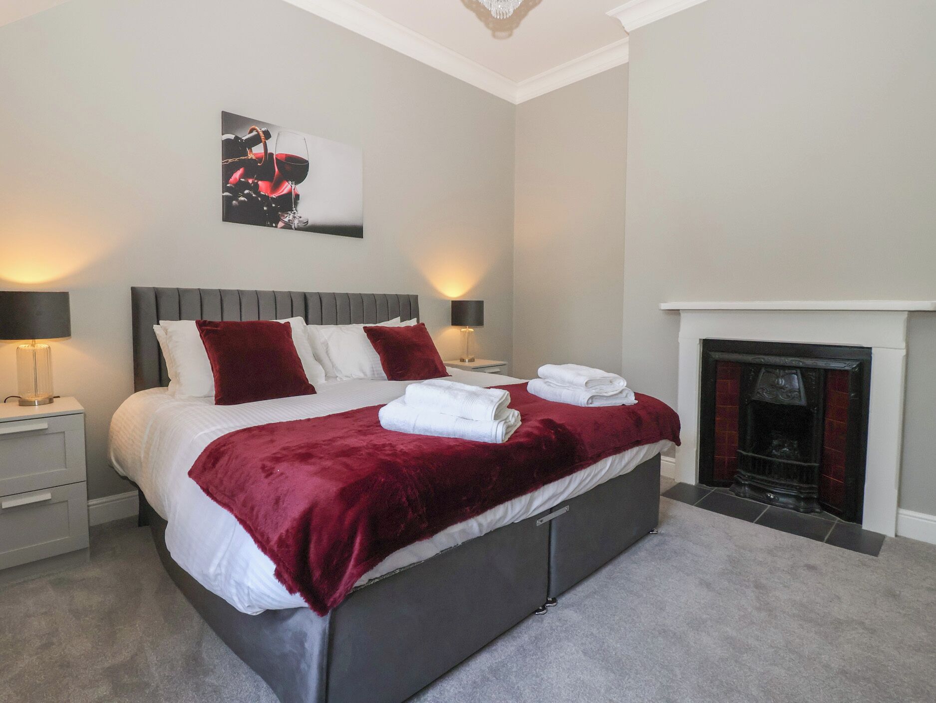 A modern bedroom with a large bed, two bedside tables, a fireplace, and a framed artwork above the bed.