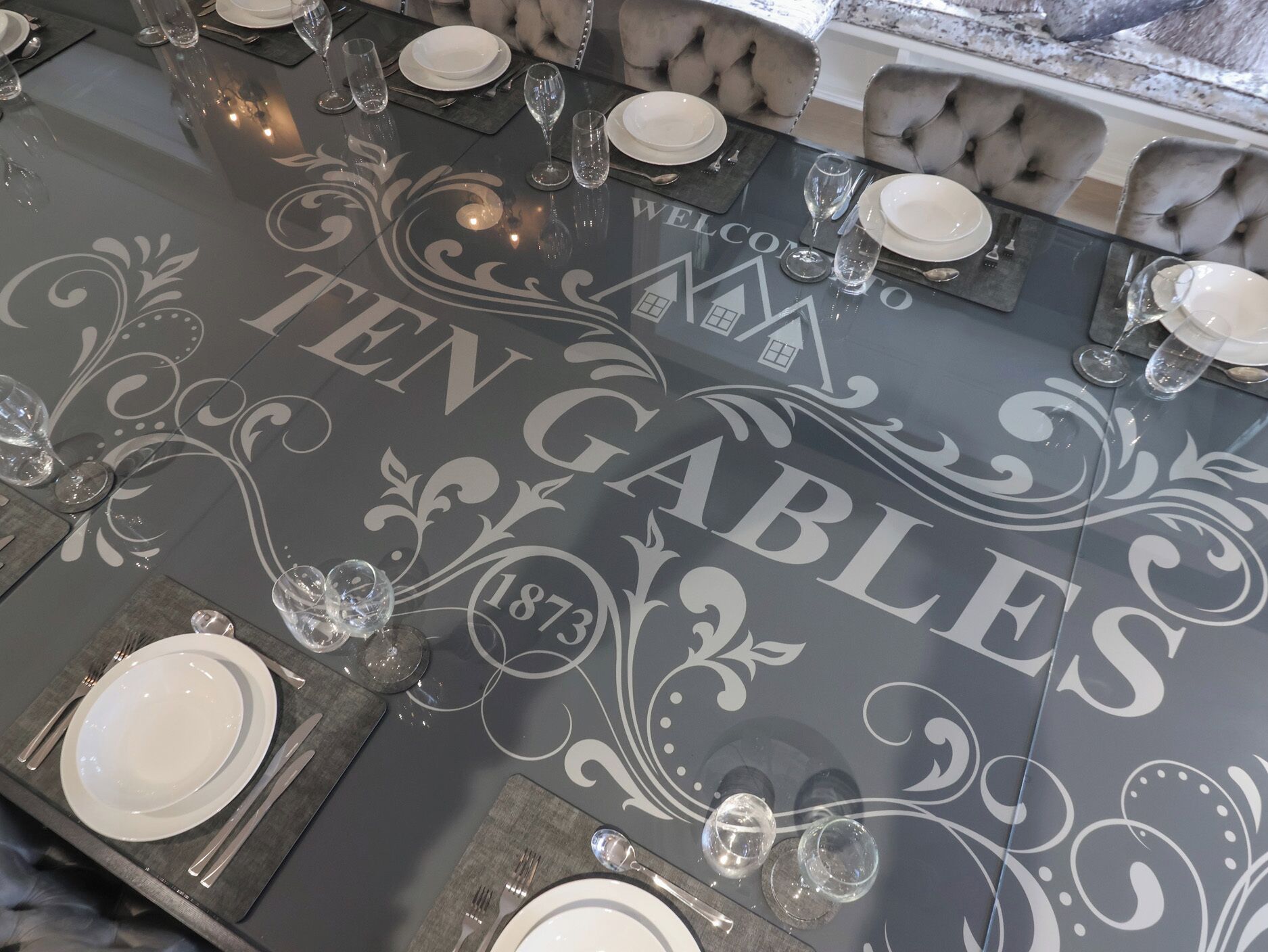A table set for a meal with a decorative tablecloth featuring the text "TEN GABLES" and the year "1873".