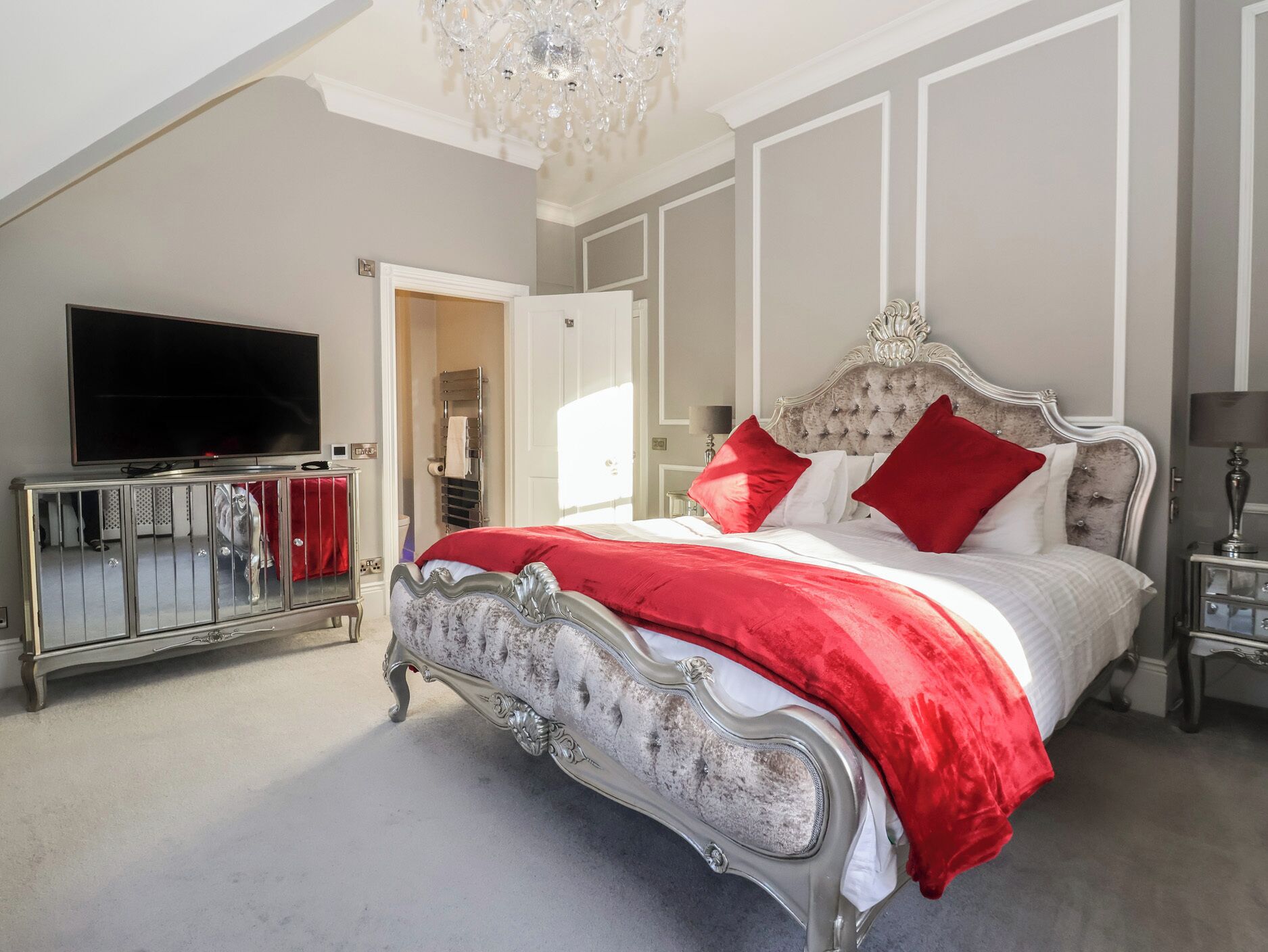 A bedroom with a large bed, a television, and a chandelier.