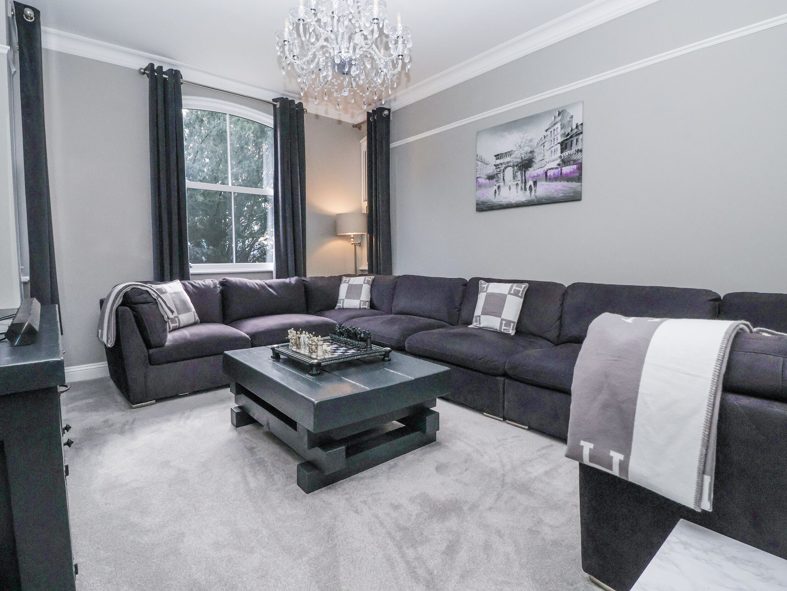 A modern living room with a sectional sofa, a coffee table, and a chandelier.