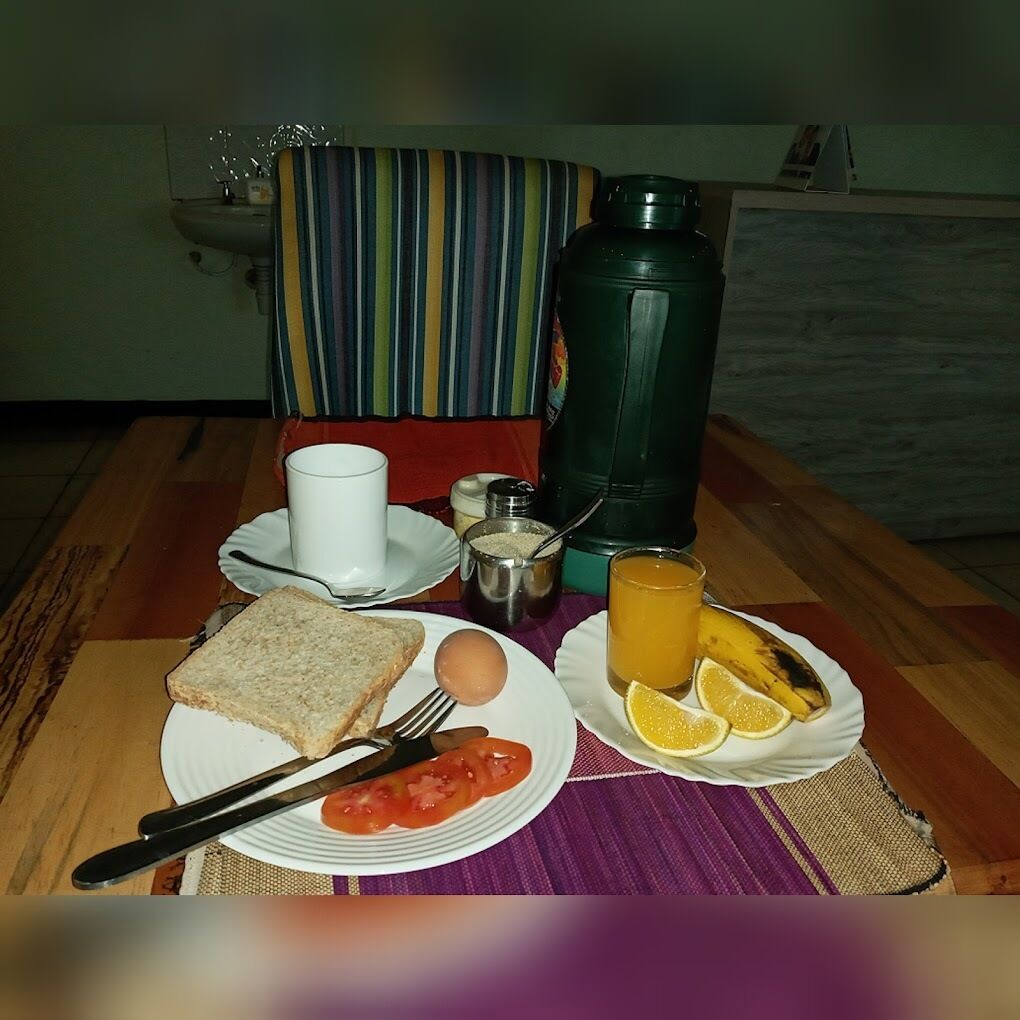 A breakfast setup with toast, egg, tomato, orange juice, and a thermos on a table.