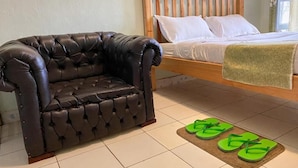 Ein Zimmer mit einer gepolsterten Ledersofa, einem hölzernen Bett mit weißer Bettwäsche und einem Paar grüner Hausschuhe auf einer Fußmatte.