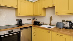 Una cocina con armarios amarillos, encimera de madera, un lavabo, una cafetera, un tostador y un lavavajillas.