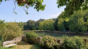 Parque junto al río con un banco, muro de piedra y abundante vegetación.