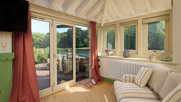 Una habitación acogedora con un amplio ventanal corredera que da a una terraza exterior, un sofá confortable y un televisor montado en la pared.