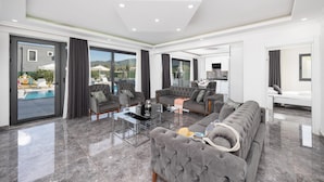 A spacious living room with a large grey sofa, a coffee table, and a view of a swimming pool and mountains. - Villa Grand Yasar 1 With 4 Bedrooms and 4 Bathrooms (Ortaca)
