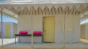Un'area salotto esterna coperta con una porta gialla, una panca con cuscino rosa e una scala che conduce all'ingresso.