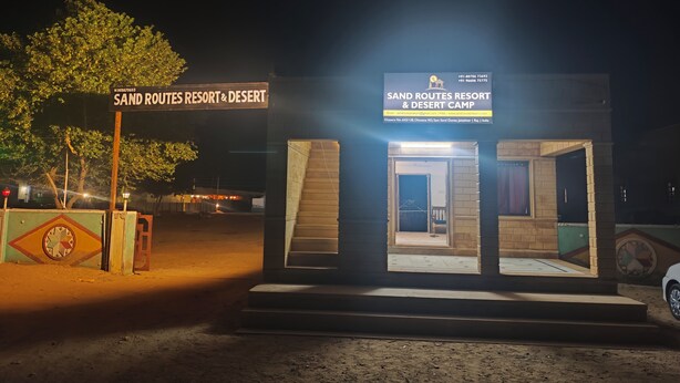 En liten, upplyst byggnad med en skylt som visar texten: ”SAND ROUTES RESORT & DESERT CAMP”.