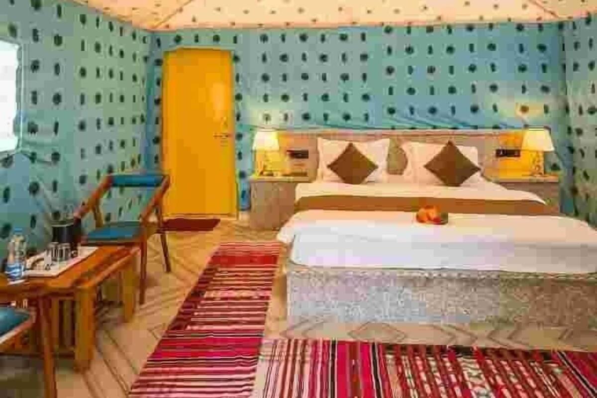 A room with a bed, a desk, and a chair. There is a window and a door.
