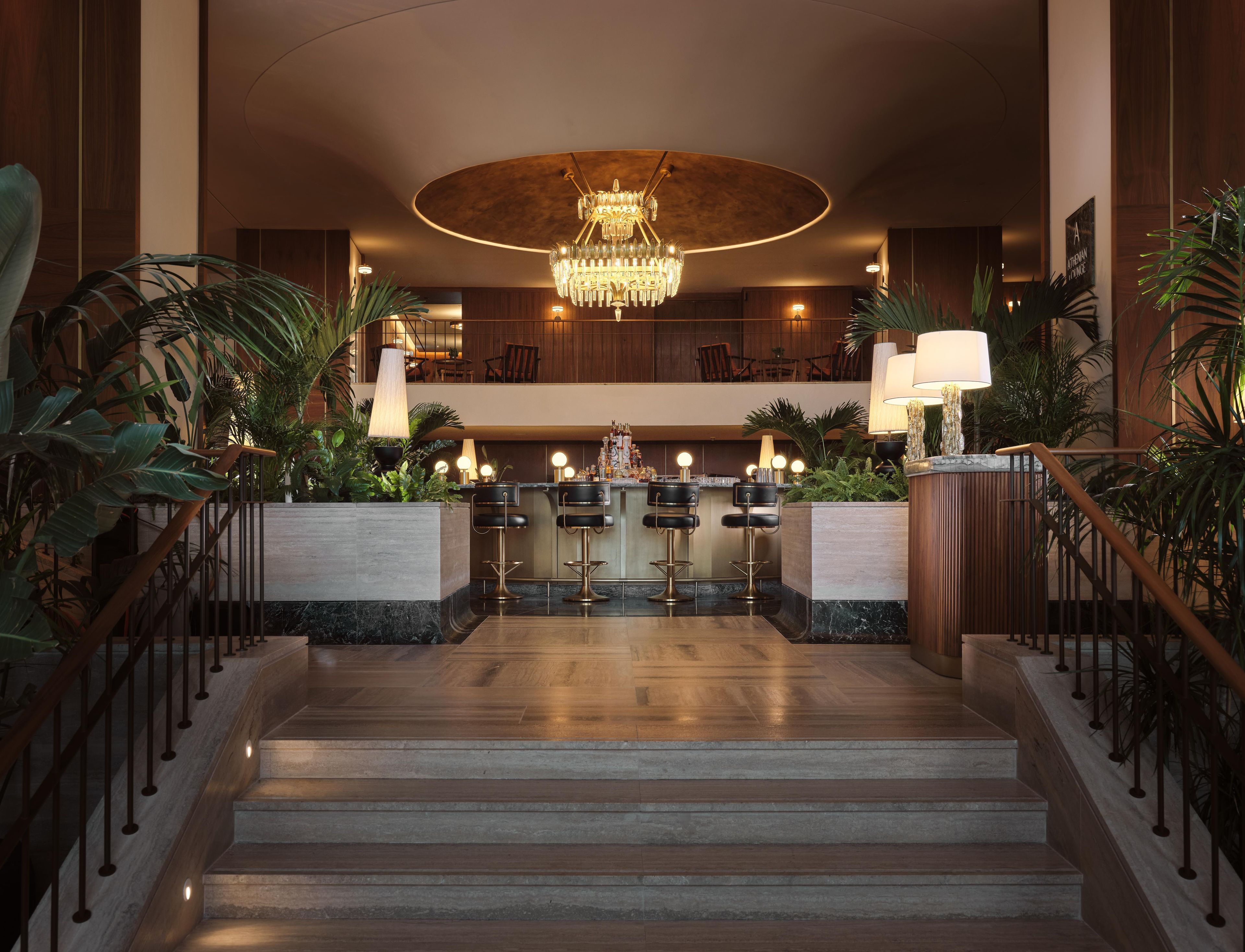 A hotel lobby with a grand chandelier, a bar area, and a staircase leading to an upper level.