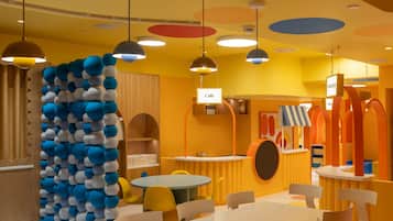 Um espaço interno vibrante, com mesas e cadeiras redondas, uma parede com design esférico azul e branco, e uma placa indicando uma área de café.