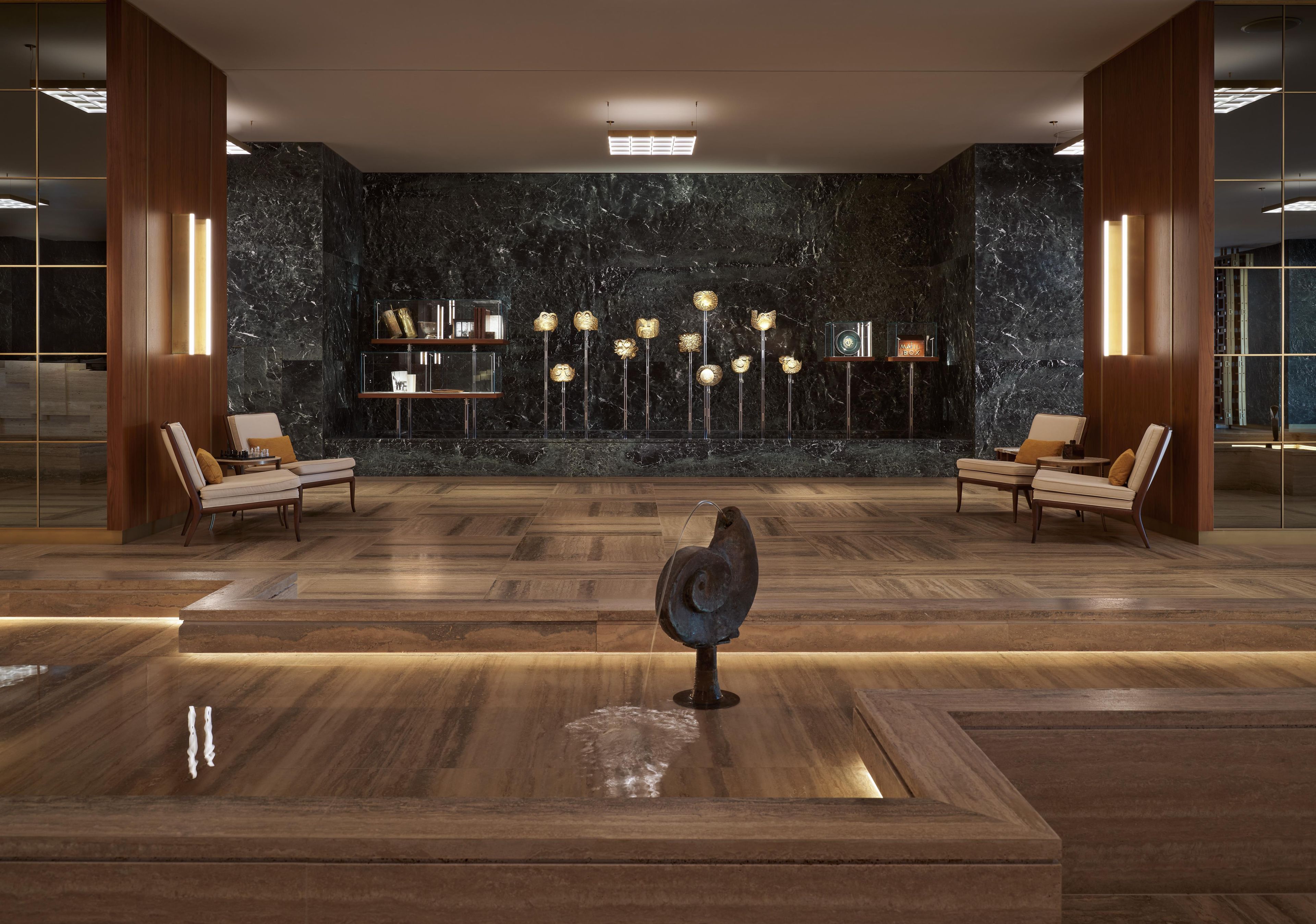A lobby with a marble wall, wooden flooring, and two seating areas with chairs.