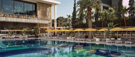 A swimming pool with lounge chairs and umbrellas, a modern building with large windows, and palm trees.