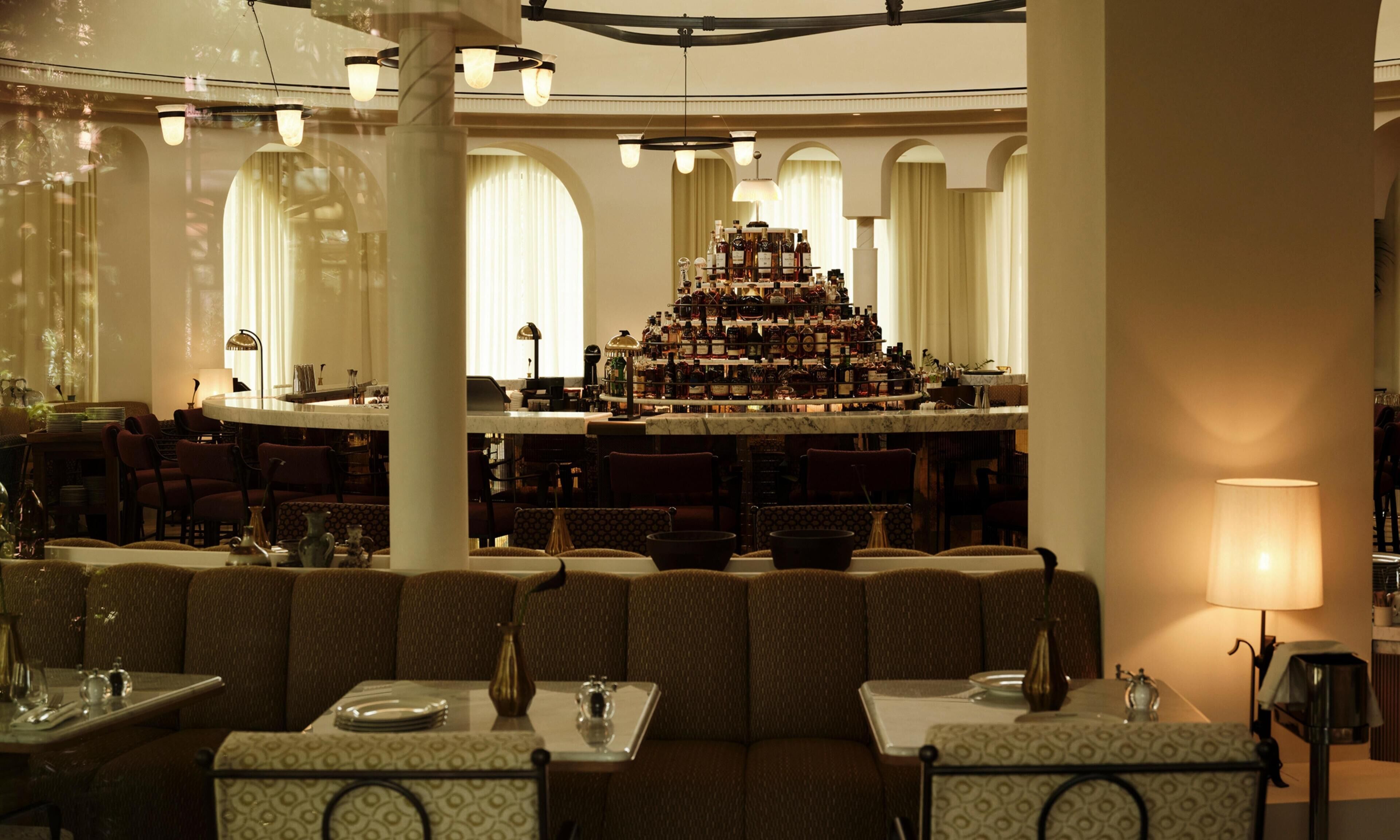 A bar area with a large display of bottles, seating with tables, and a chandelier.