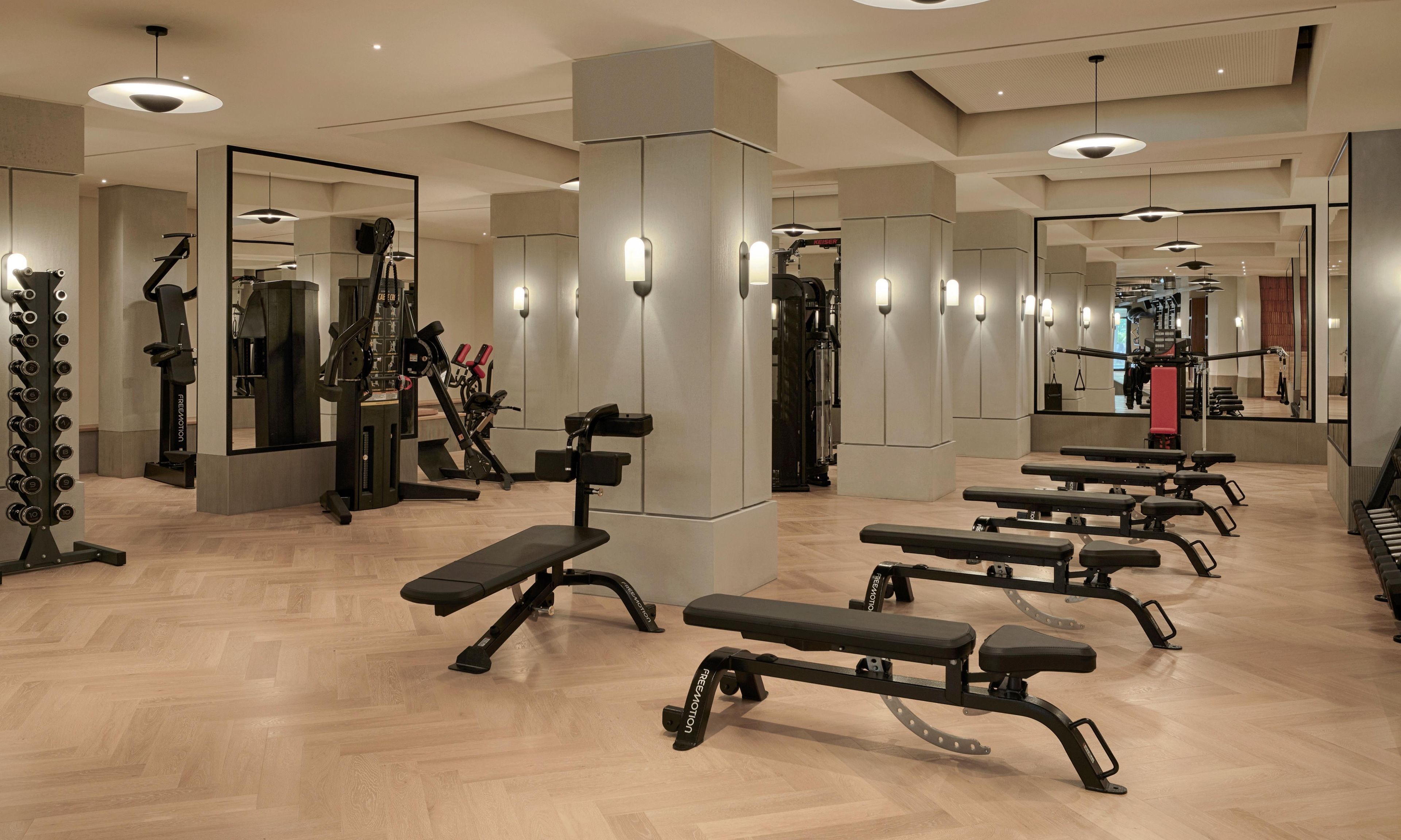 A gym with exercise equipment, benches, and mirrors.