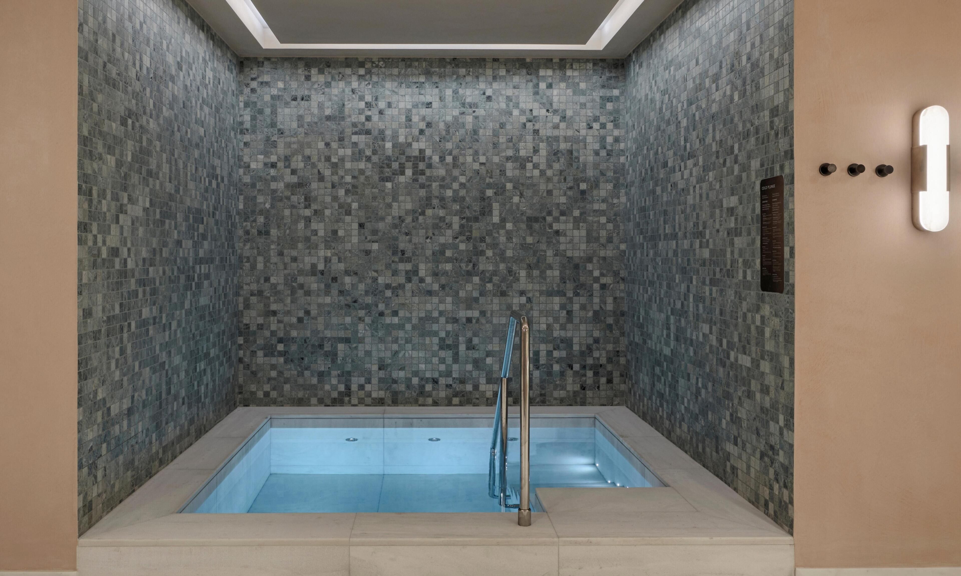 Un baño moderno con pared de azulejos, bañera con mampara de vidrio e iluminación montada en la pared.