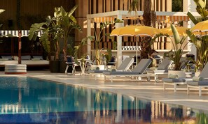 A poolside area with lounge chairs, umbrellas, and potted plants. - Conrad Athens The Ilisian (Athens)