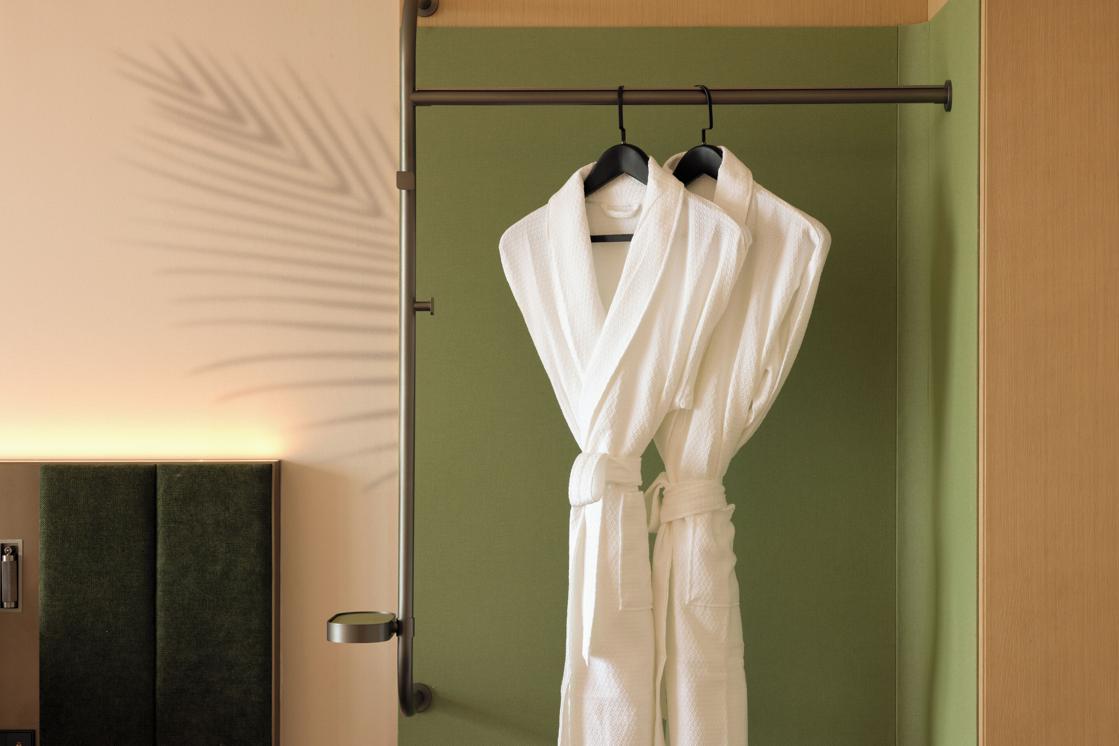 Un baño con pared verde, un perchero con dos albornoces blancos y una puerta de madera.
