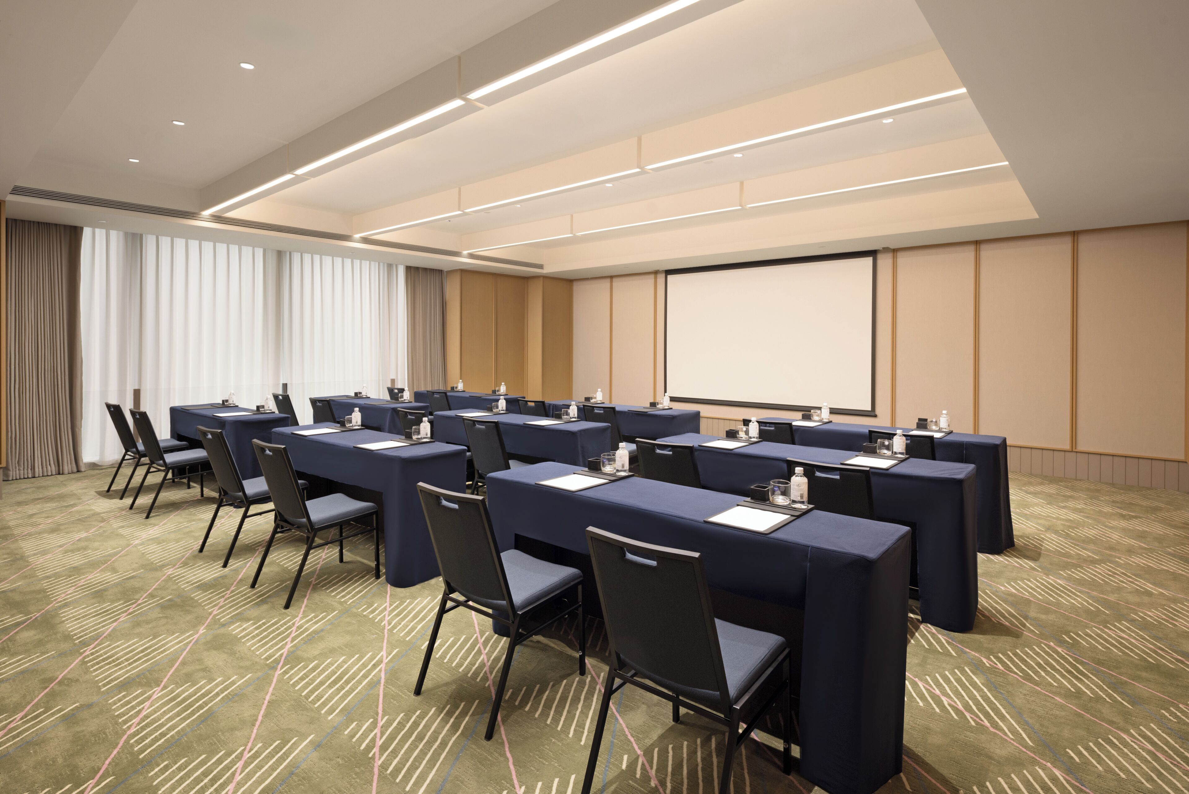 A conference room with multiple tables and chairs, a projector screen, and a carpeted floor.