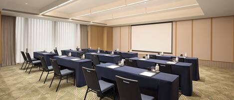 A conference room with multiple tables and chairs, a projector screen, and a carpeted floor.