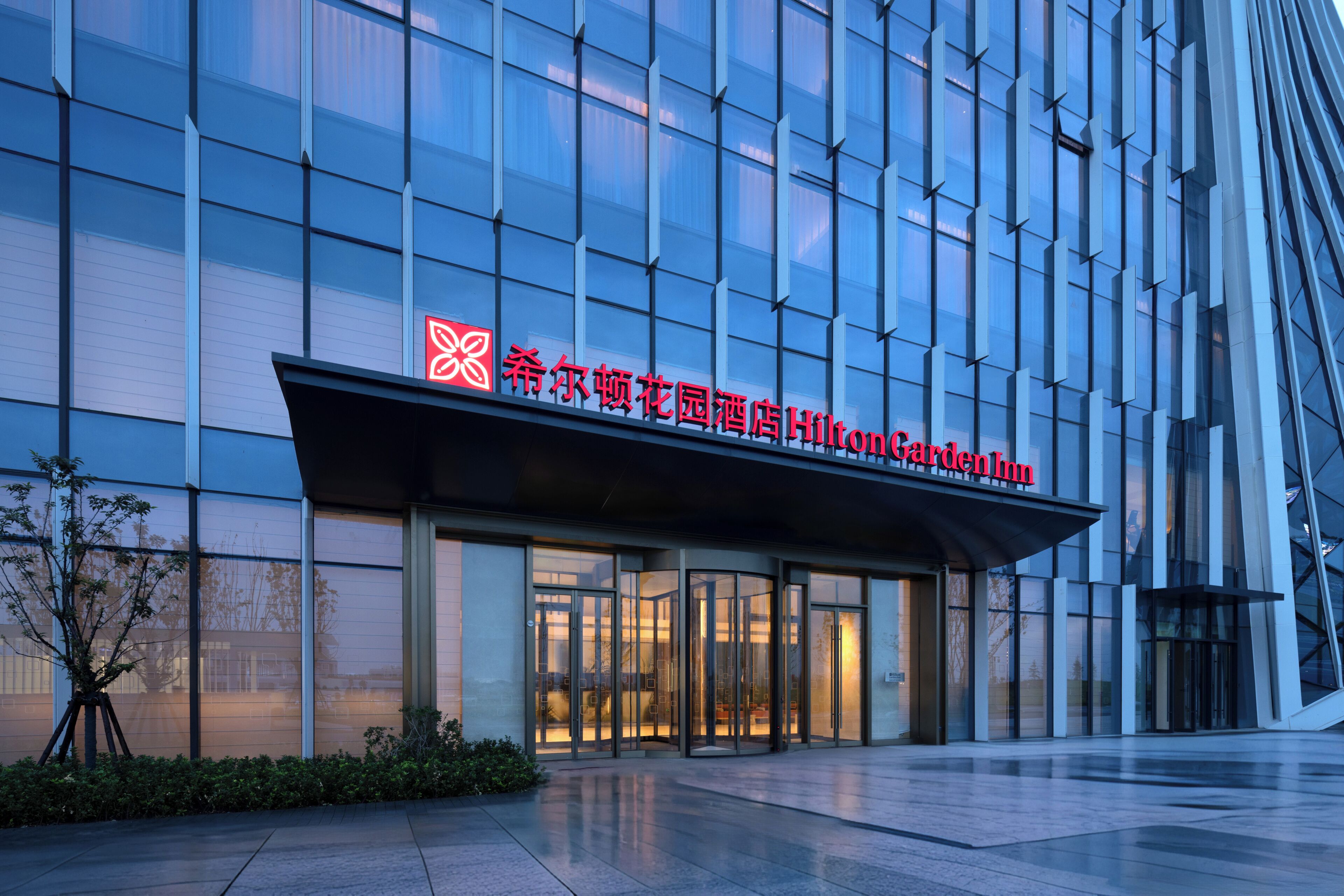 A modern hotel with a glass facade and a sign indicating it is the Hilton Garden Inn.