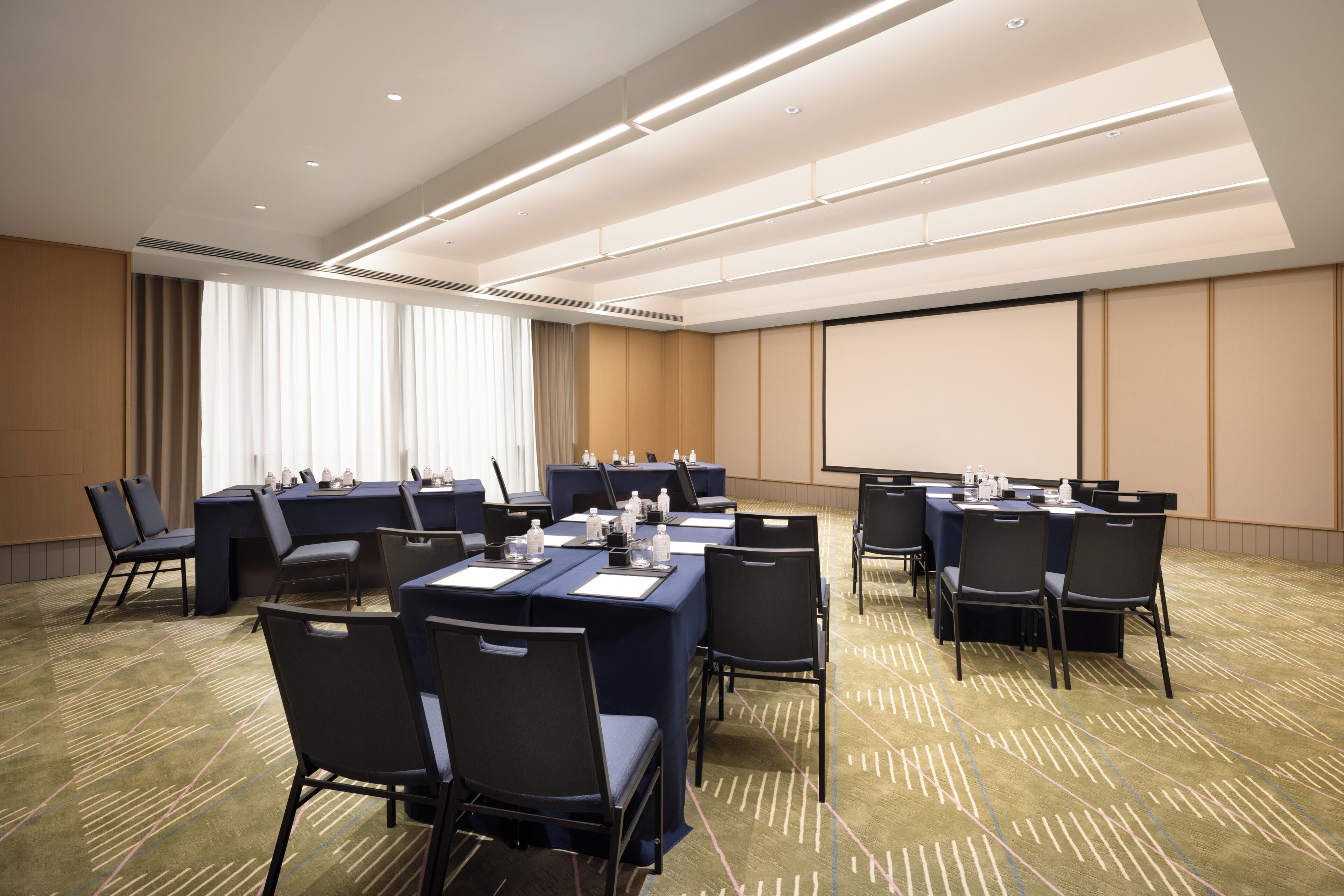 Un salón de conferencias con varias mesas, sillas y una pantalla de proyección.