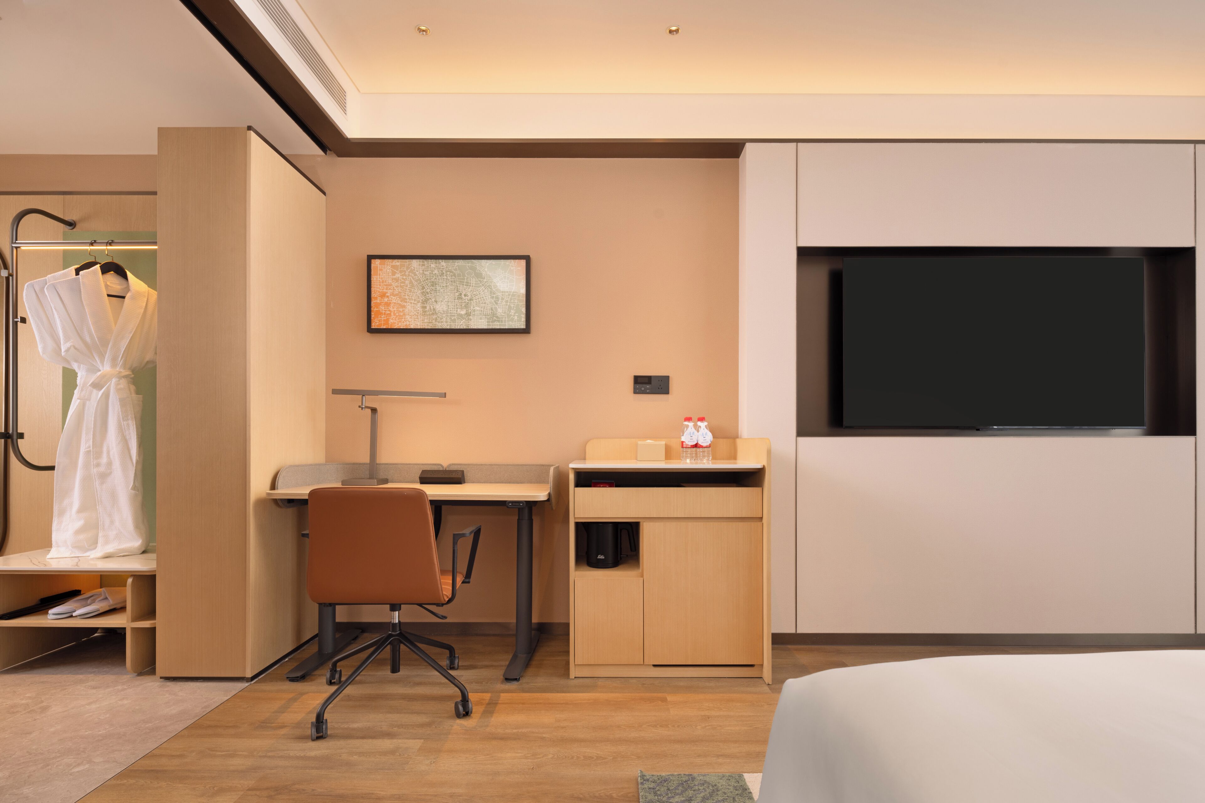 Une chambre d’hôtel comprenant un lit, un bureau avec une chaise, une télévision, un peignoir et un porte-manteau.