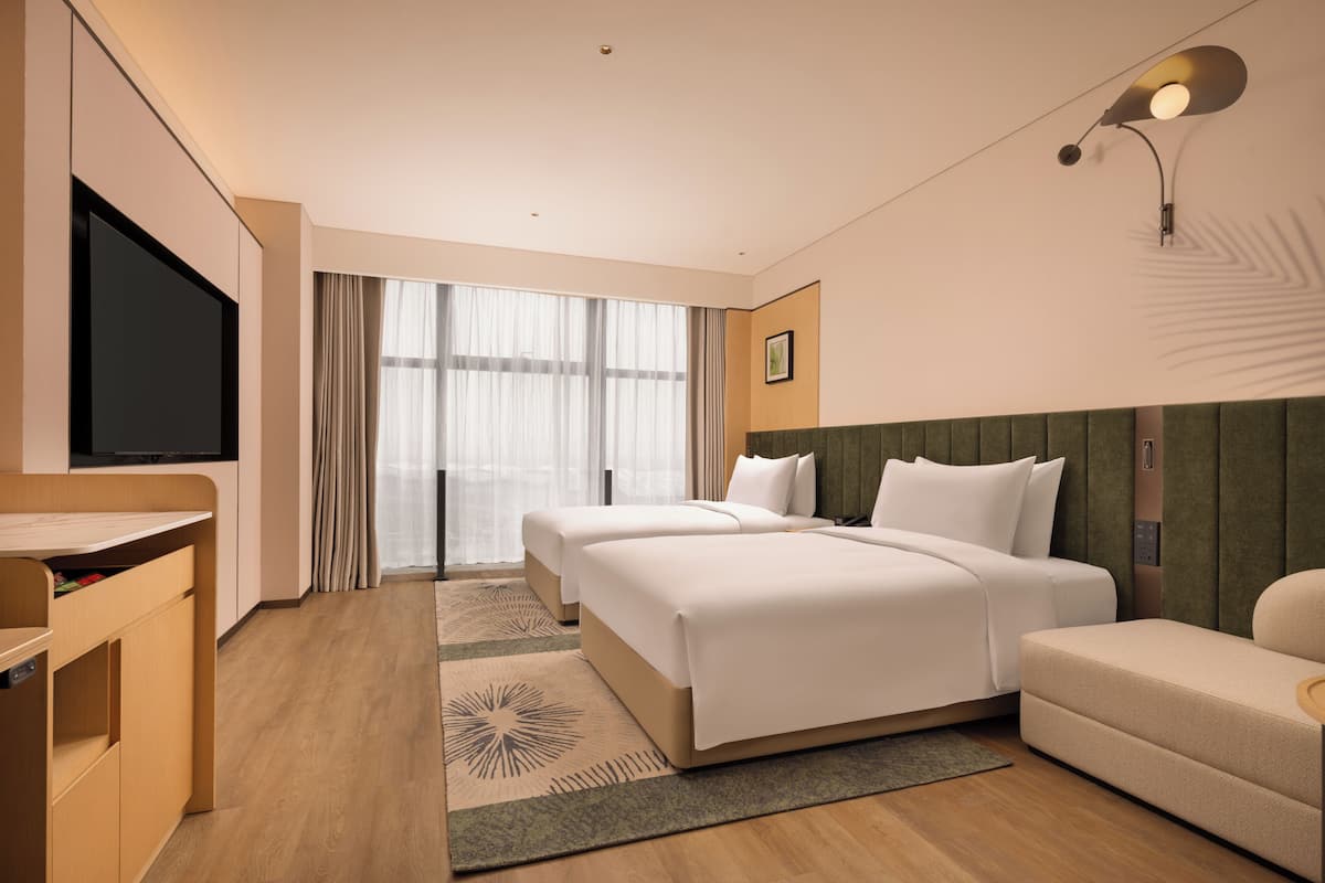 A hotel room with a large flat-screen TV, two beds, a desk, and a sofa.