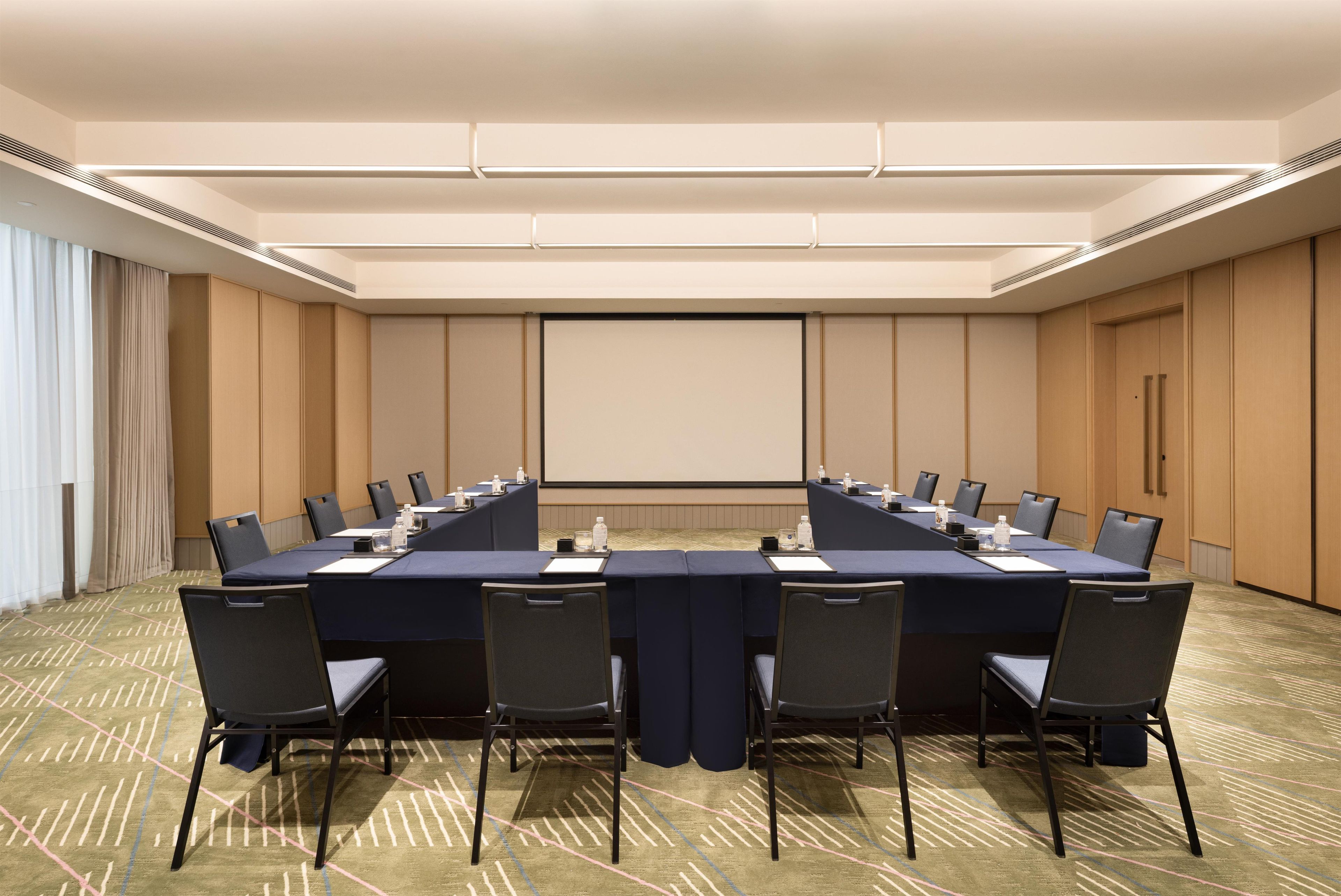 Une salle de conférence avec une longue table, des chaises, un écran de projection et un sol recouvert de moquette.