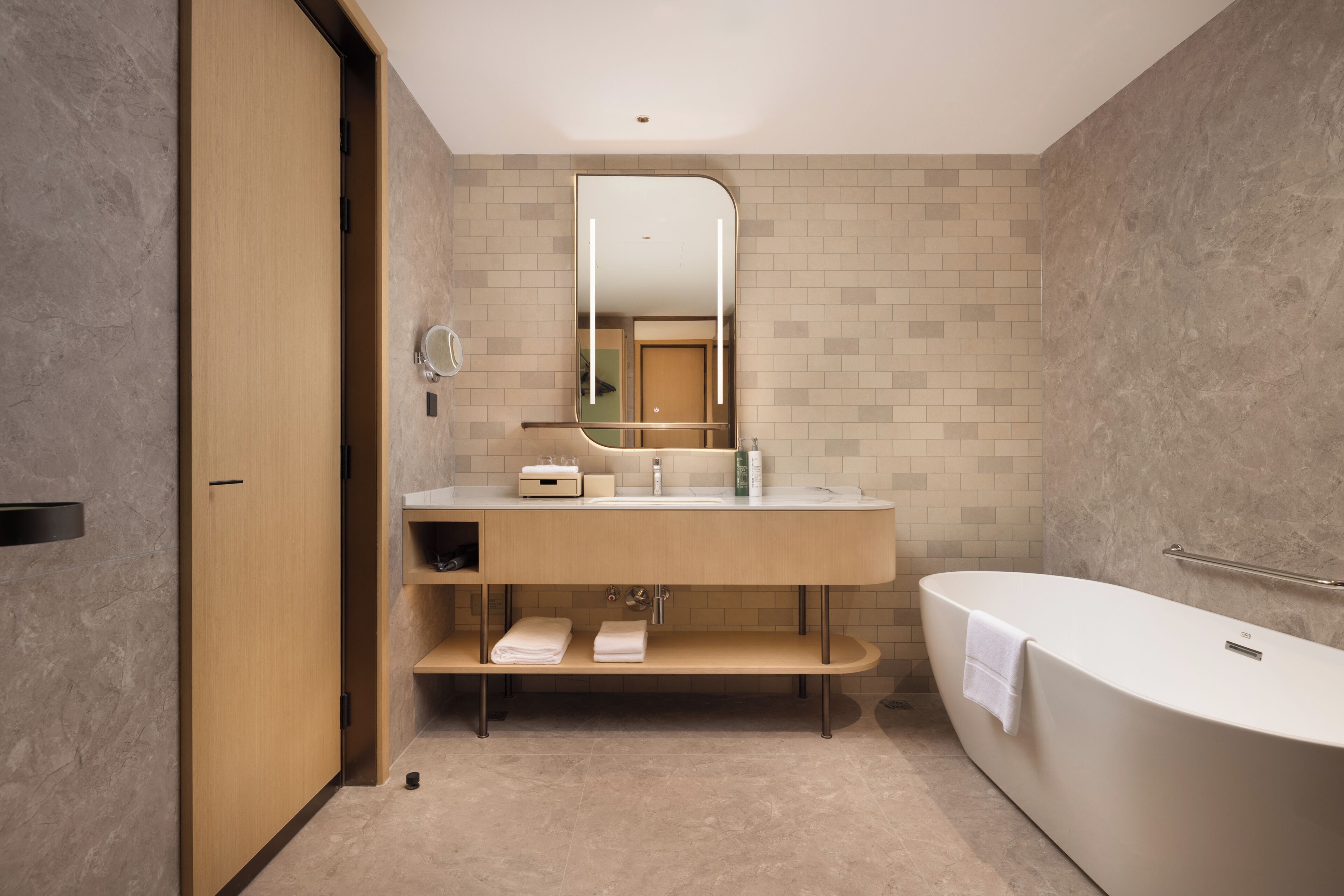 A modern bathroom with a wooden vanity, a large mirror, a bathtub, and a towel rack.