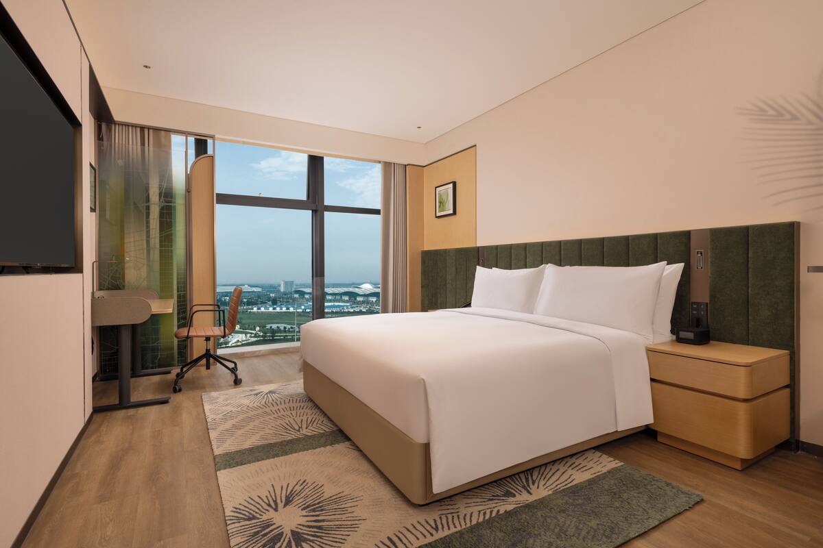 A hotel room with a large bed, a desk, a chair, a nightstand, and a TV.