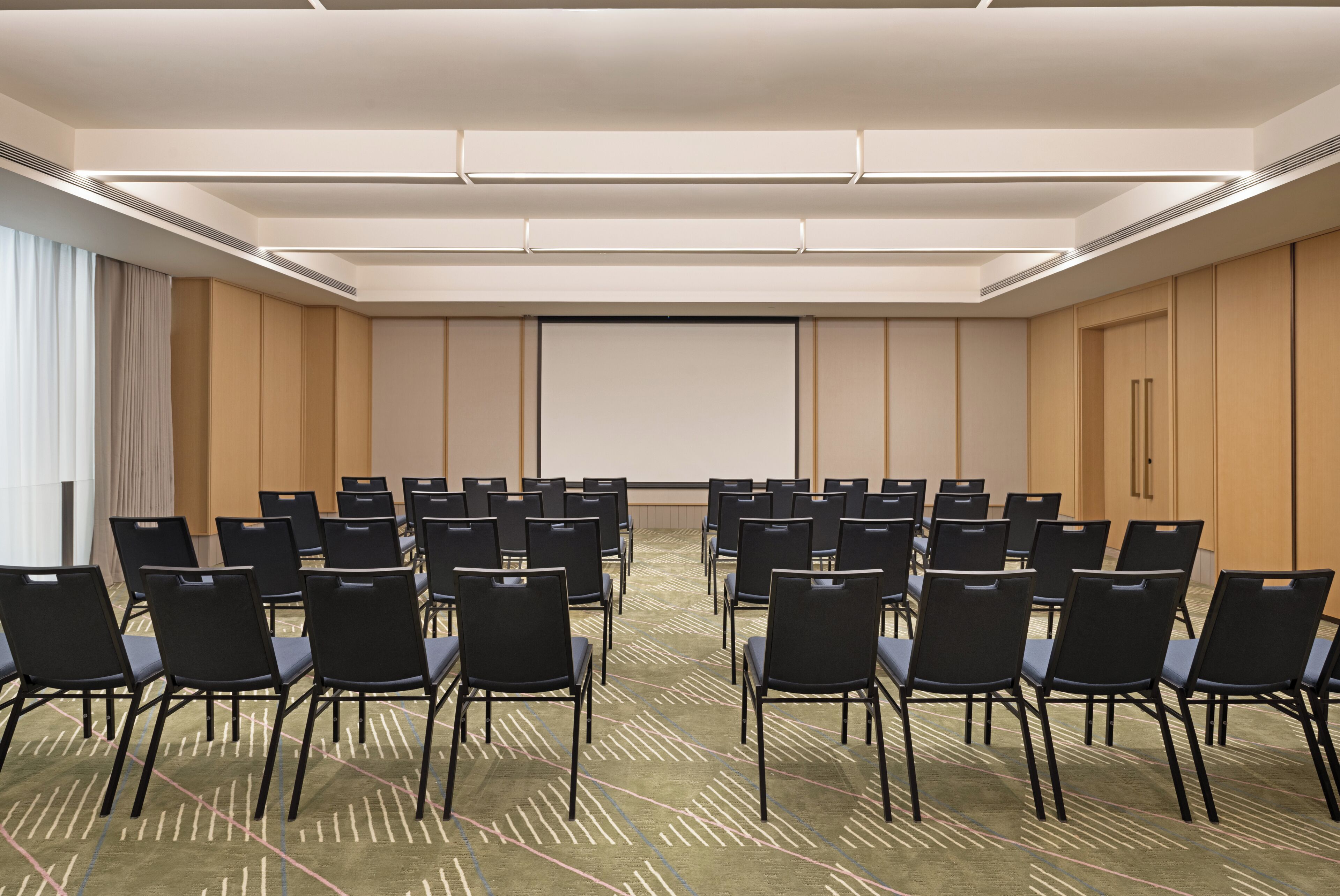 A conference room with rows of chairs, a projector screen, and a carpeted floor.