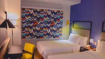 A hotel room with two beds, a desk, a chair, and a colorful chevron-patterned wall.