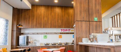 Interior moderno de restaurante con paneles de madera, una barra con platos y sillas anaranjadas y rojas.