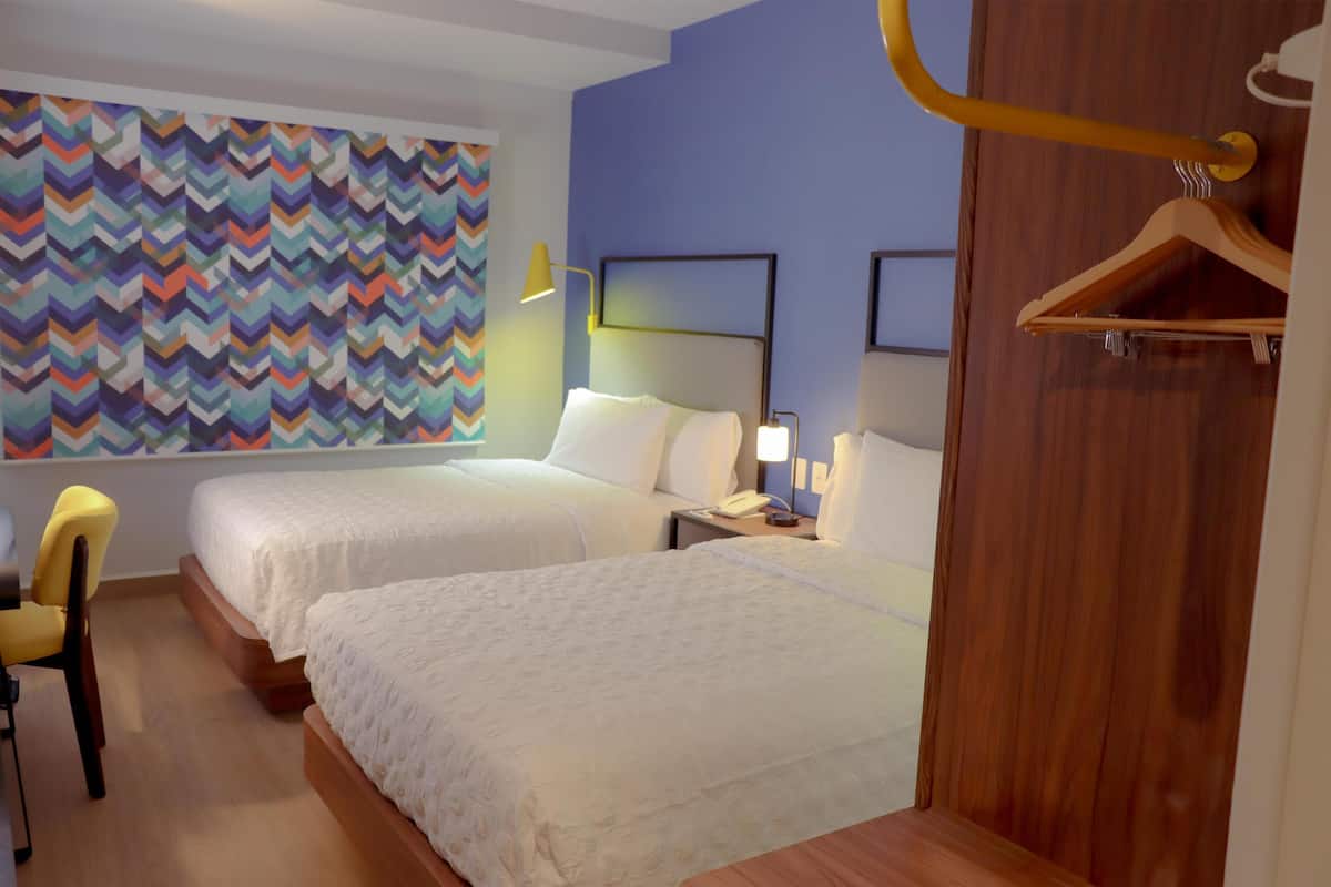 Una habitación de hotel con dos camas, un escritorio, una silla, un muro colorido y un armario de madera.