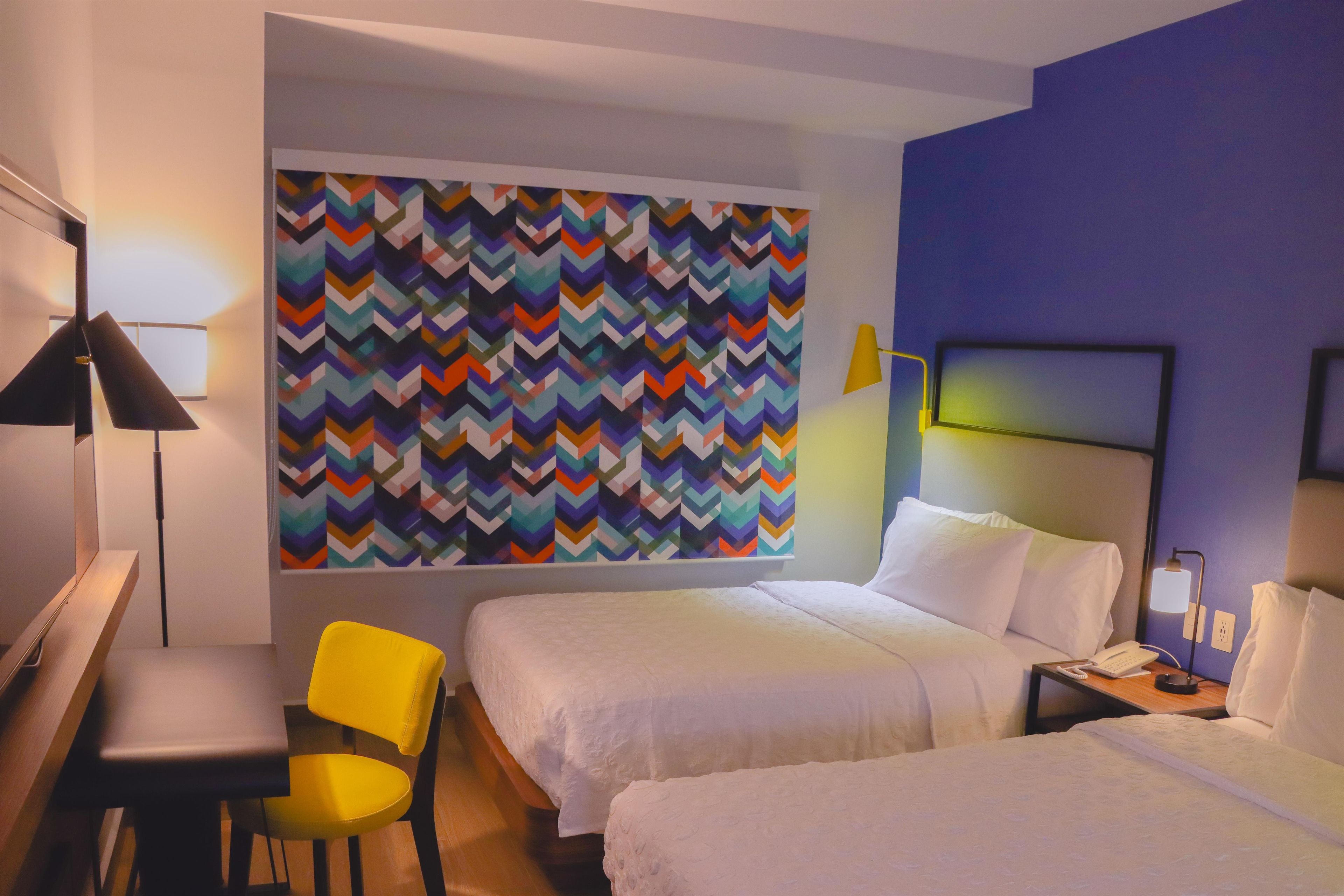 Habitación de hotel con dos camas, un escritorio, una silla y una pared con llamativo estampado de rombos.