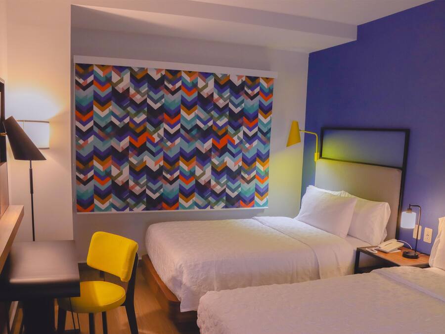 Habitación de hotel con dos camas, un escritorio, una silla y una pared con llamativo estampado de rombos.