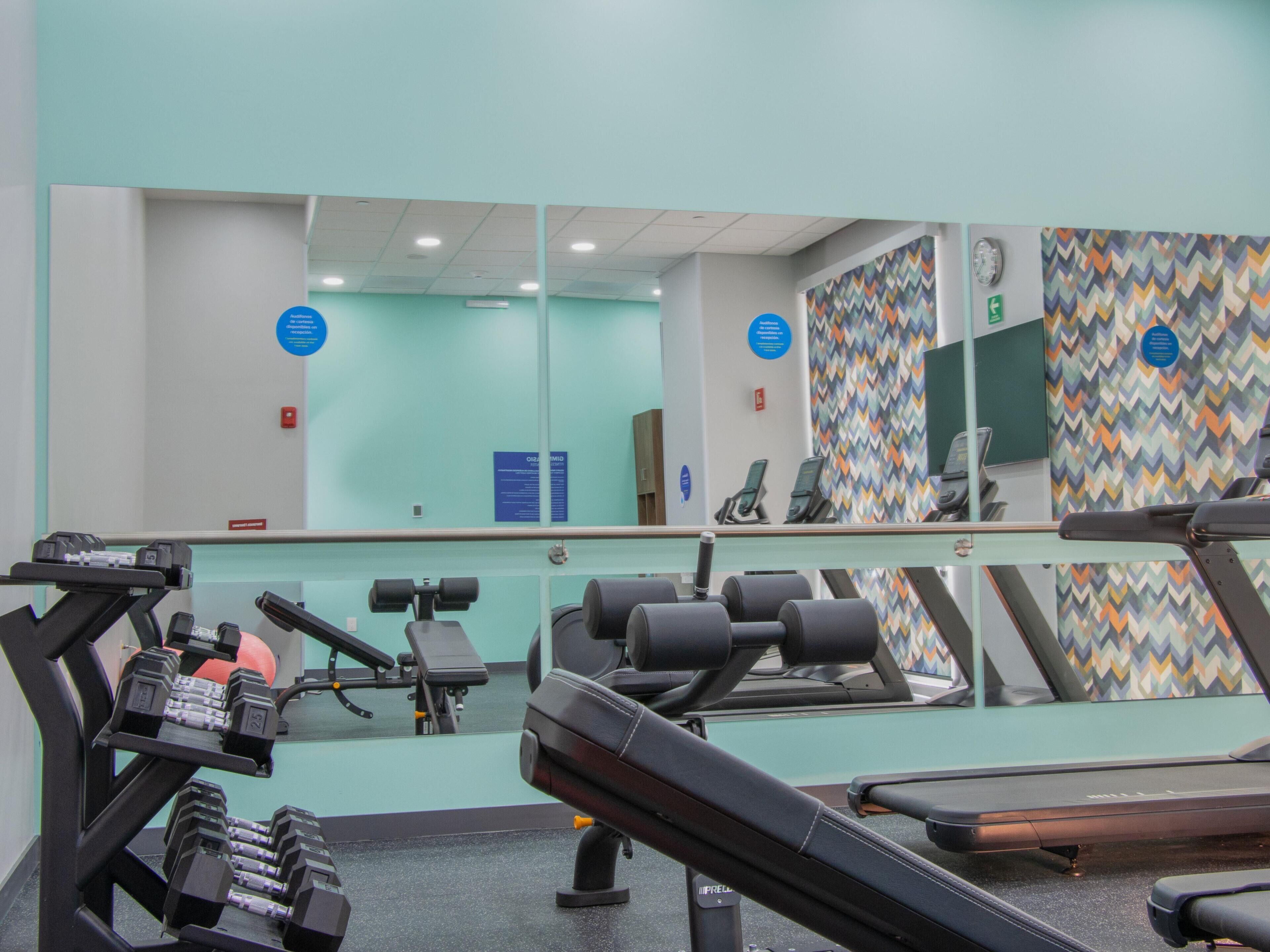 Een fitnessruimte met trainingsapparatuur, een spiegelwand en een behang.