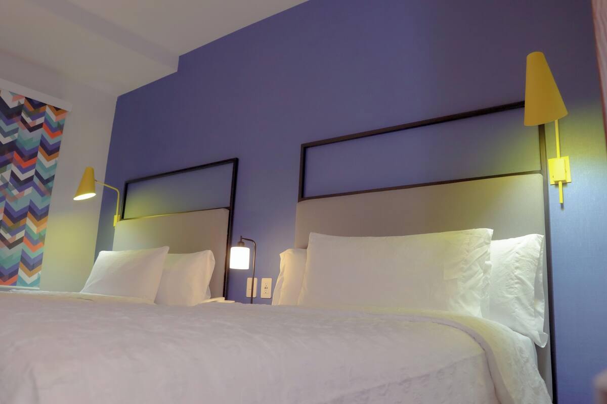 Una habitación de hotel con una cama, dos mesitas de noche, una lámpara y una pared con un diseño en zigzag.