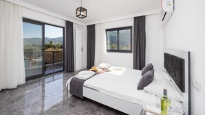 A modern bedroom with a large bed, a balcony with a view of the mountains, and a ceiling light fixture. - Villa Grand Yasar 4 With 4 Bedrooms and 4 Bathrooms (Ortaca)