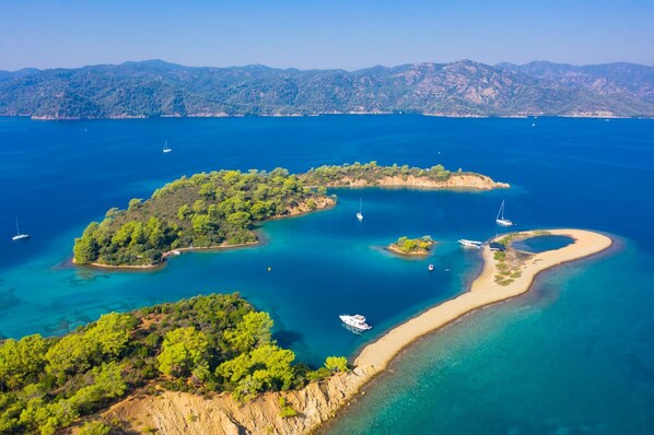 An aerial view of a coastal area with clear blue waters, several small islands, and boats.