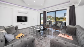 A modern living room with grey sofas, a glass coffee table, and a flat-screen TV mounted on the wall. - Villa Grand Yasar 4 With 4 Bedrooms and 4 Bathrooms (Ortaca)