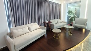Una sala de estar moderna con un sofá, dos mesitas auxiliares y un gran ventanal con cortinas.