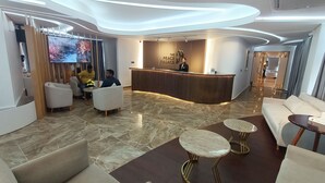 Un moderno vestíbulo de hotel con mostrador de recepción, zona de estar y una pantalla grande mostrando una escena natural.