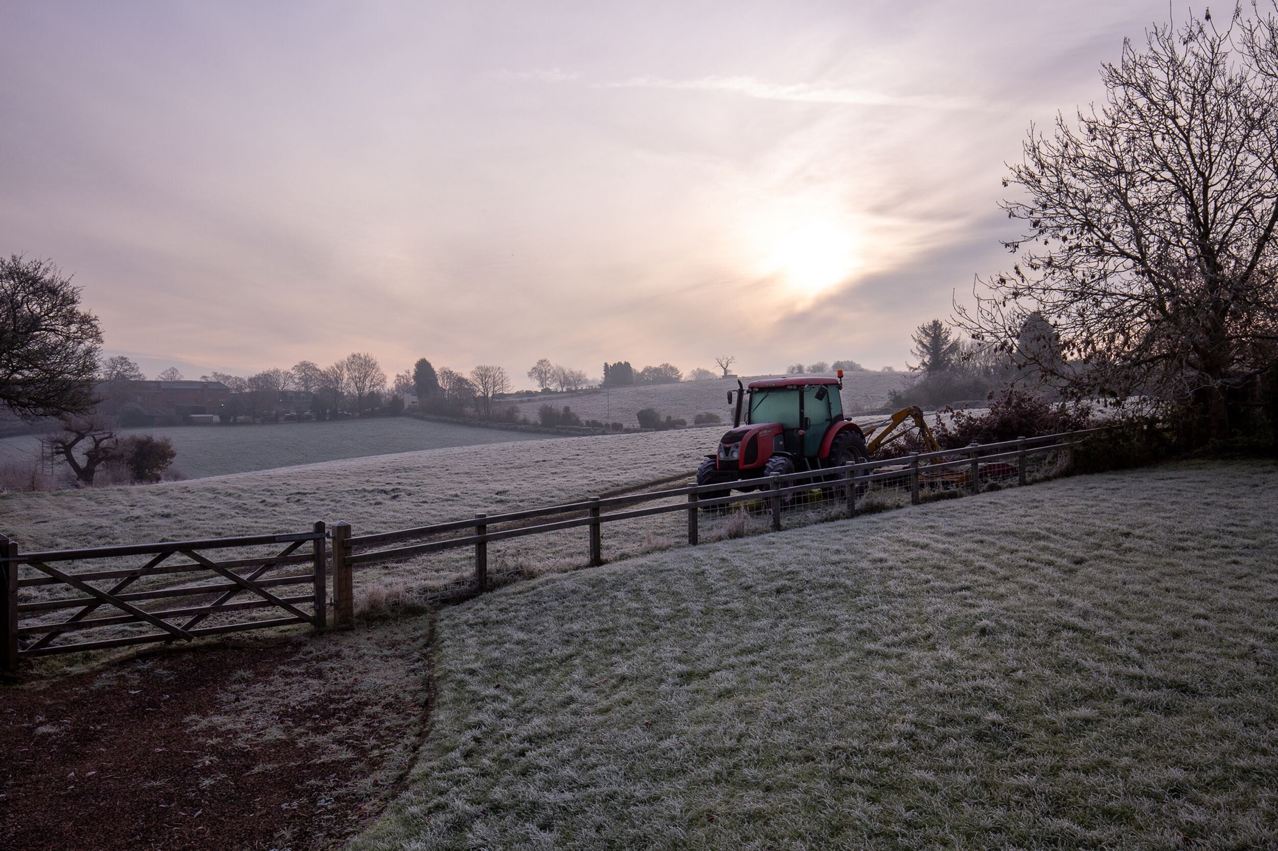 Een bevroren landschap met een tractor nabij een houten poort.